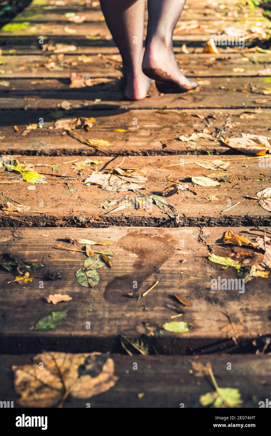 Donna che cammina a piedi nudi attraverso un ponte di legno nella foresta Foto Stock