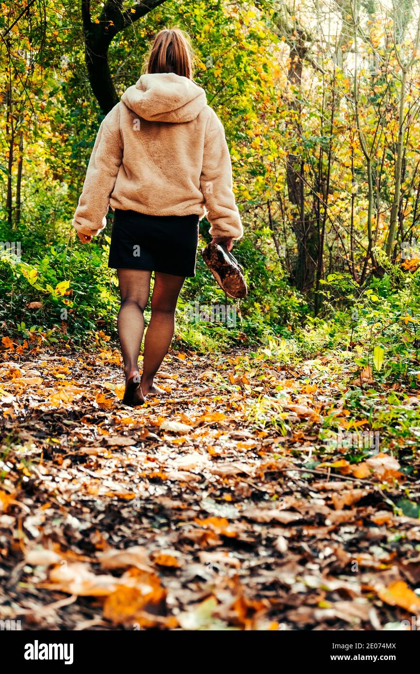 Donna che cammina a piedi nudi attraverso la foresta che tiene i suoi allenatori Foto Stock