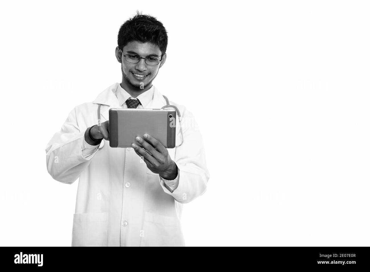 Studio shot di giovani felici uomo indiano medico sorridere mentre usando tavoletta digitale Foto Stock