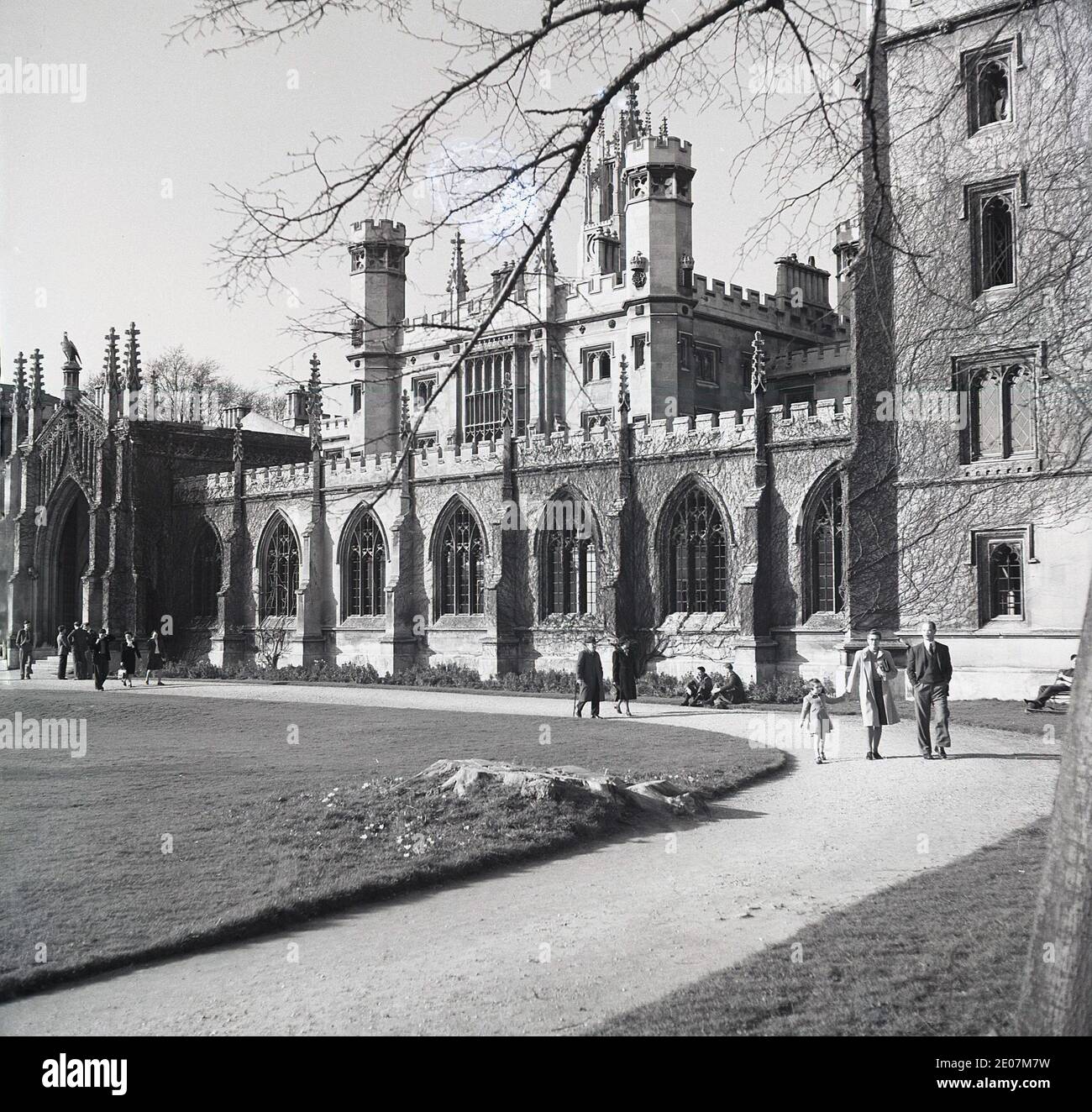 Anni '50, storico, nei terreni del college, le persone che camminano lungo un percorso accanto agli edifici eleganti e storici, alla Cambridge University, Cambridge, Inghilterra, Regno Unito. Foto Stock