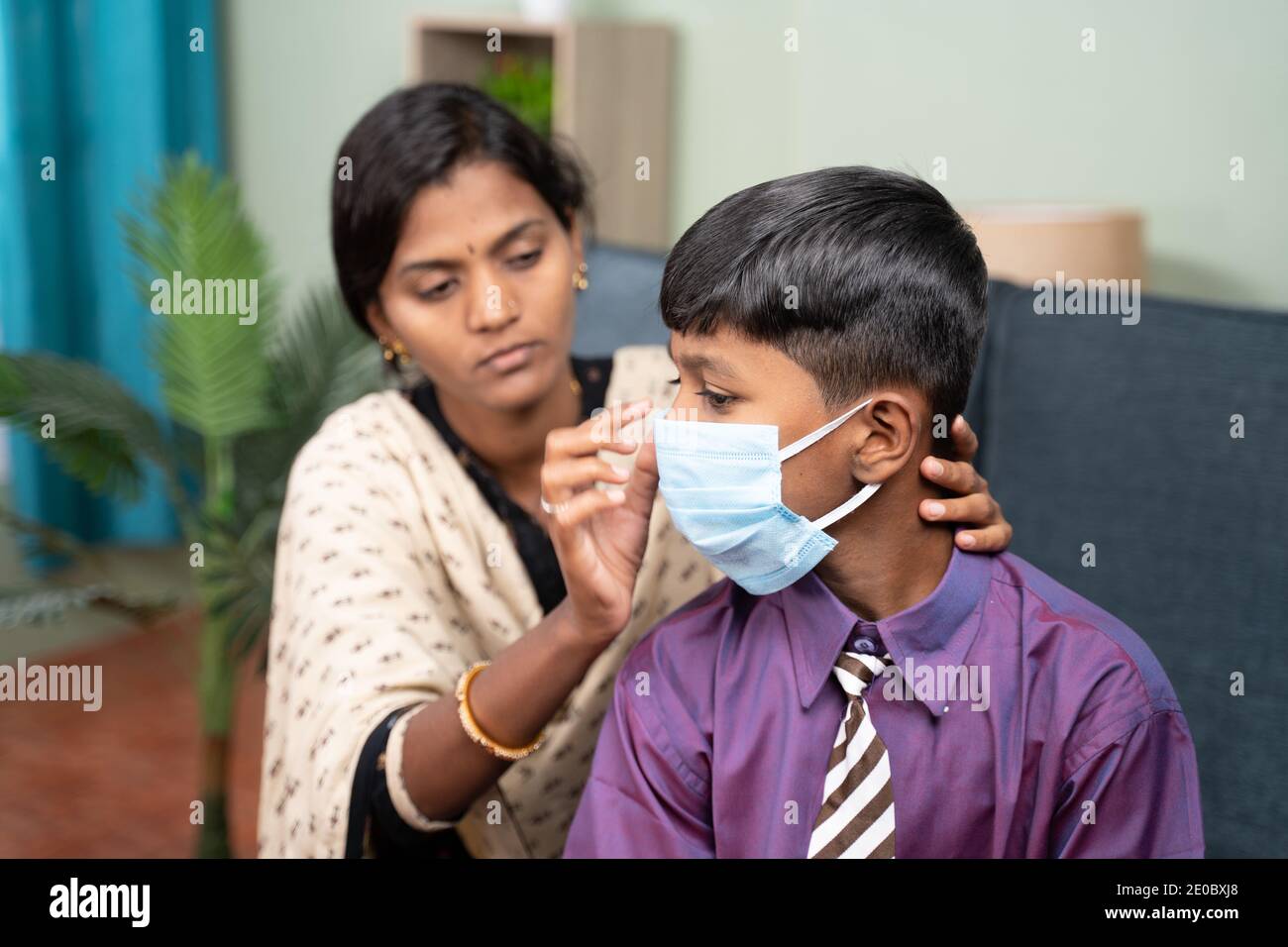 Madre che aiuta suo figlio a indossare la maschera facciale prima di andare a scuola a casa come coronavirus covid-19 misure di sicurezza sanitaria. Foto Stock