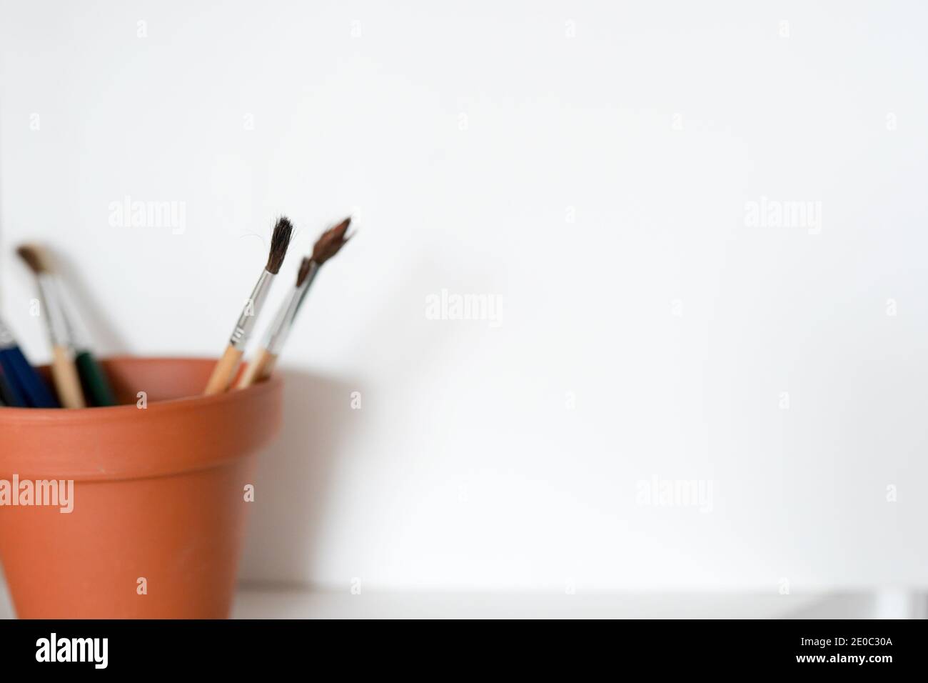 Una pentola di artisti dipinge pennelli in una pentola marrone su uno sfondo bianco. Spazio per la copia disponibile. Foto Stock