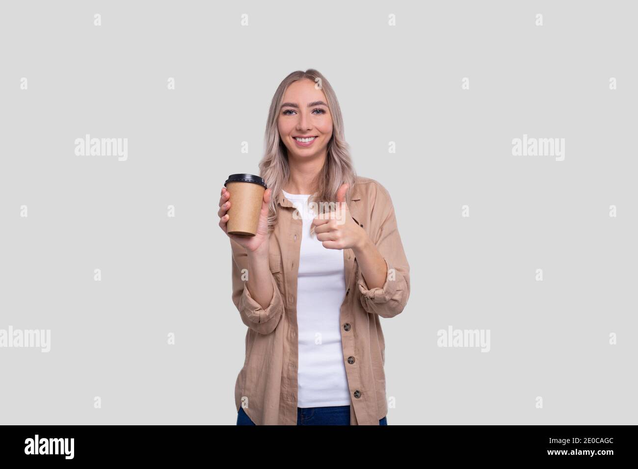 Girl Holding Take Away Coffee Cup mostrando Thumb Up. Ragazza con la tazza di caffè da andare in mani. Foto Stock