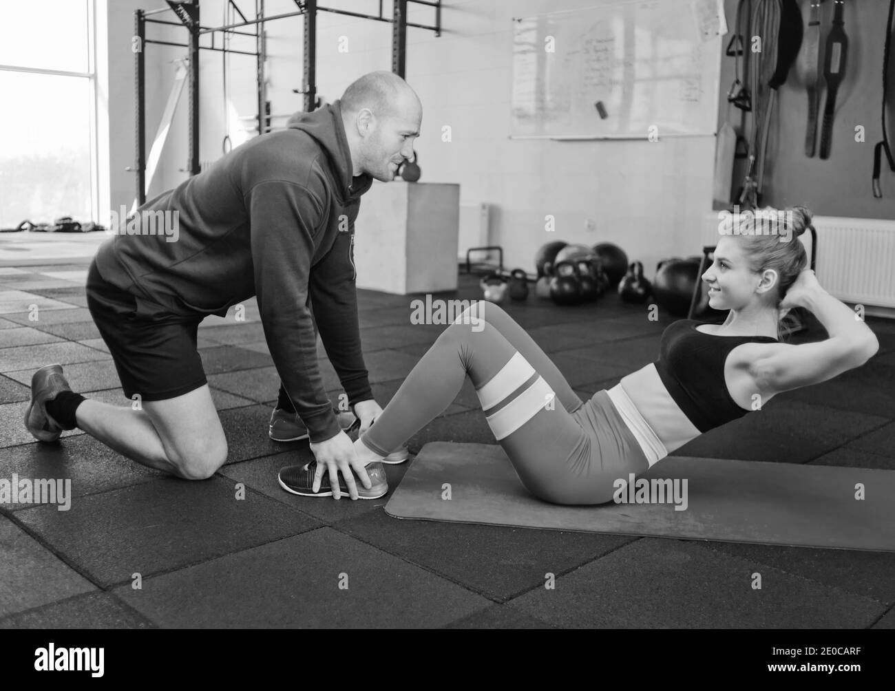 L'uomo sta tenendo le gambe della donna che sta facendo l'esercitazione torcente per i muscoli addominali che si trovano sul tappetino in palestra. Foto Stock