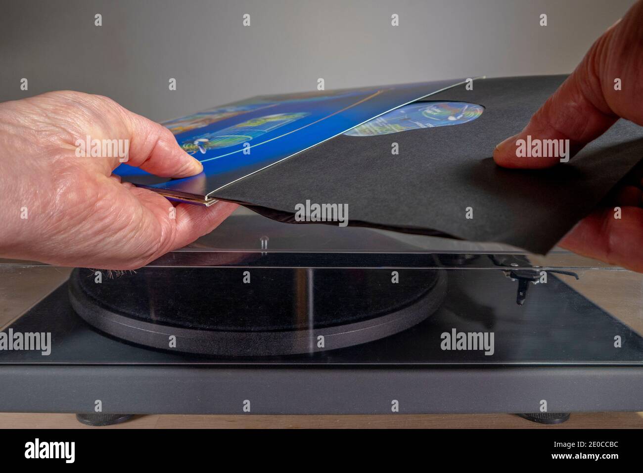 Primo piano POV di un uomo che fa scivolare fuori una manica di carta, tenendo un album in vinile LP, dalla copertina di cartone, sopra un giradischi / lettore di dischi. Foto Stock