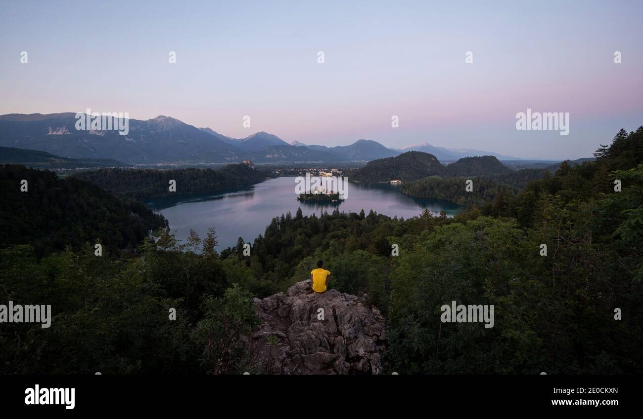 Giovane uomo che gode di vista panoramica tramonto sul Lago Bled Island Blejsko jezero da Osojnica punto panoramico collina superiore carniolan Julian alpi Montagne in Slov Foto Stock