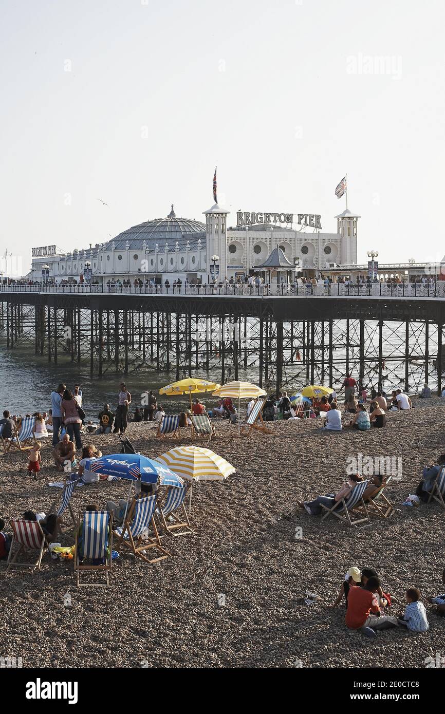 GRAN BRETAGNA / Inghilterra / Peopel seduto alla spiaggia di Brighton con Brighton Pier dietro Foto Stock
