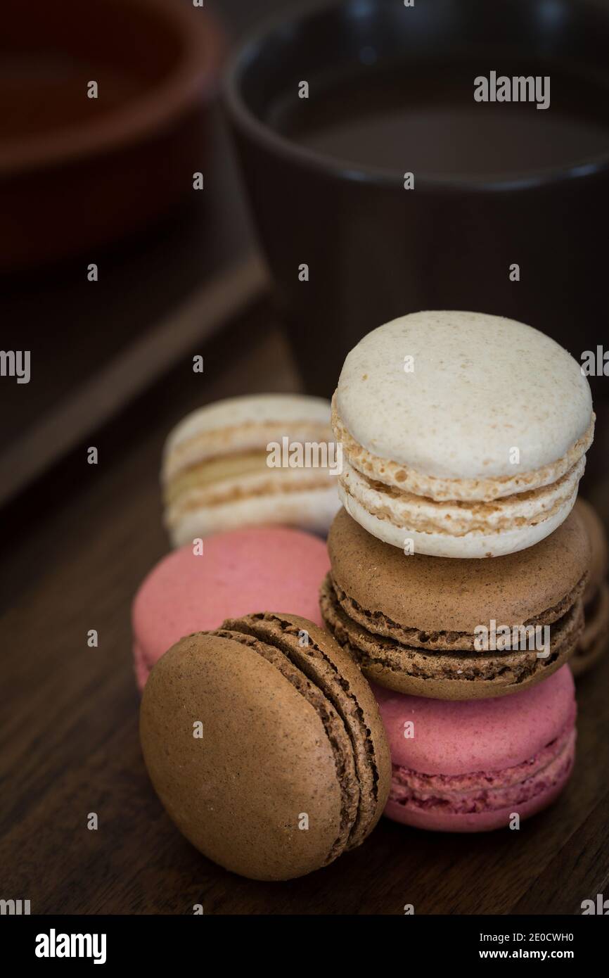 Un primo piano di una pila di macaron o Macaron colorati tra cui rosa, cioccolato e vaniglia con una tazza di caffè Foto Stock