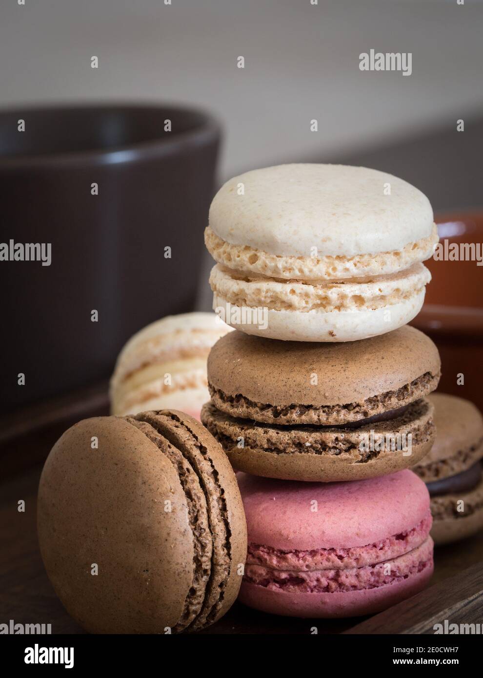 Un primo piano di una pila di macaron o Macaron colorati tra cui rosa, cioccolato e vaniglia con una tazza di caffè Foto Stock
