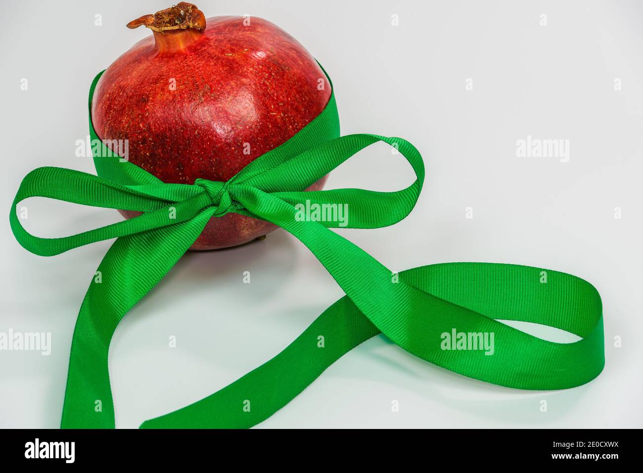 Un melograno con un nastro verde come regalo di nuovo anno su sfondo bianco. Frutta fresca rossa con decorazione ornamentale verde e spazio copia. Foto Stock
