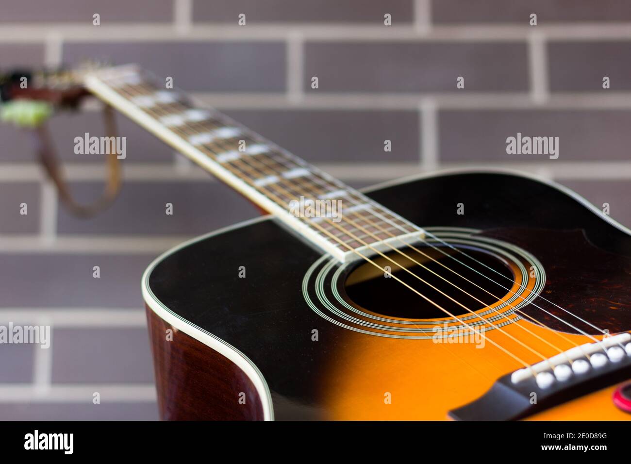 Chitarra acustica nera e arancione su fondo muretto in mattoni. Focus su buca e corde del suono. Industria musicale, concetti di business dell'intrattenimento Foto Stock