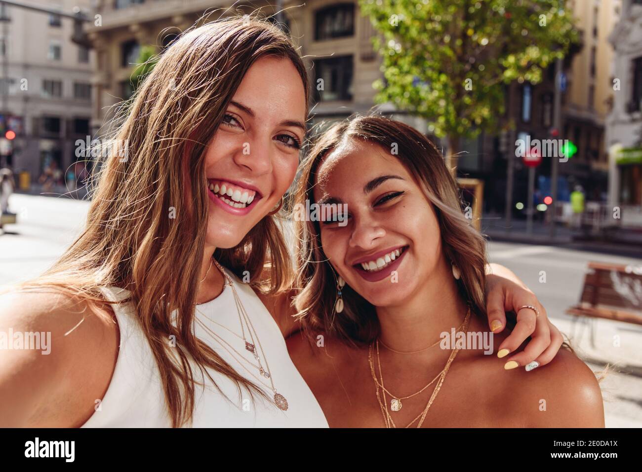 Allegro giovane femmina amici abbracciare felice mentre prendendo selfie sopra piazza urbana nel giorno d'estate Foto Stock