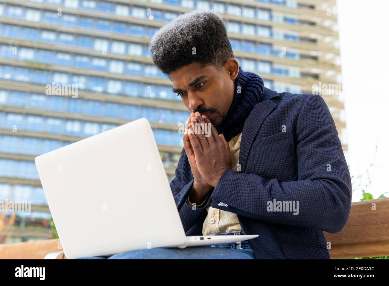 Basso angolo di imprenditore africano americano maschile seduto sulla strada con occhi chiusi e pugnalati mentre si lavora su un computer portatile e in attesa di approvazione Foto Stock
