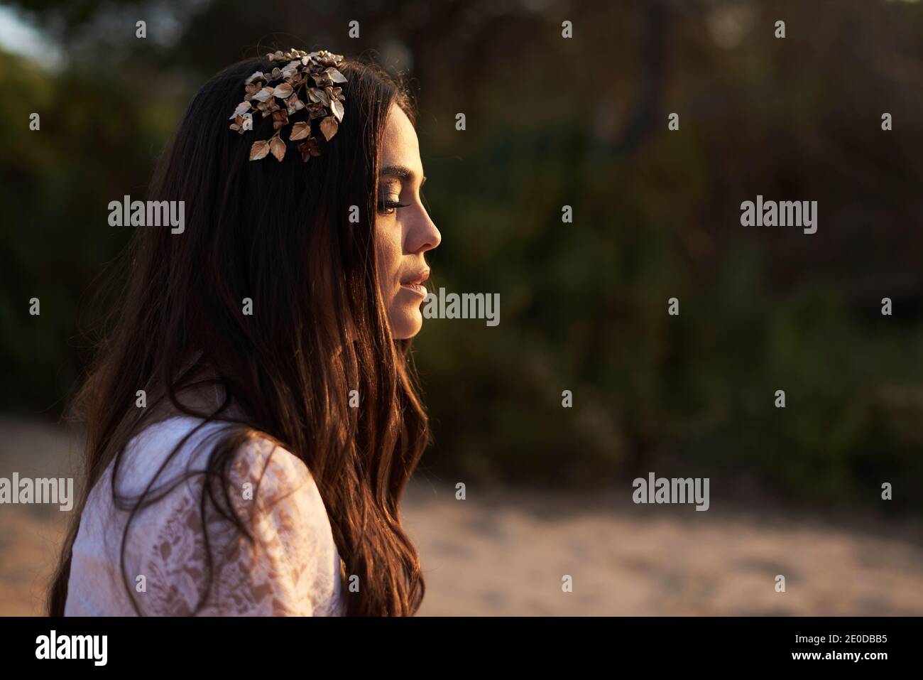 Vista laterale di elegante giovane femmina in boho bridal maxi vestitevi e cavatoie in boschi verdi e guardate via Foto Stock
