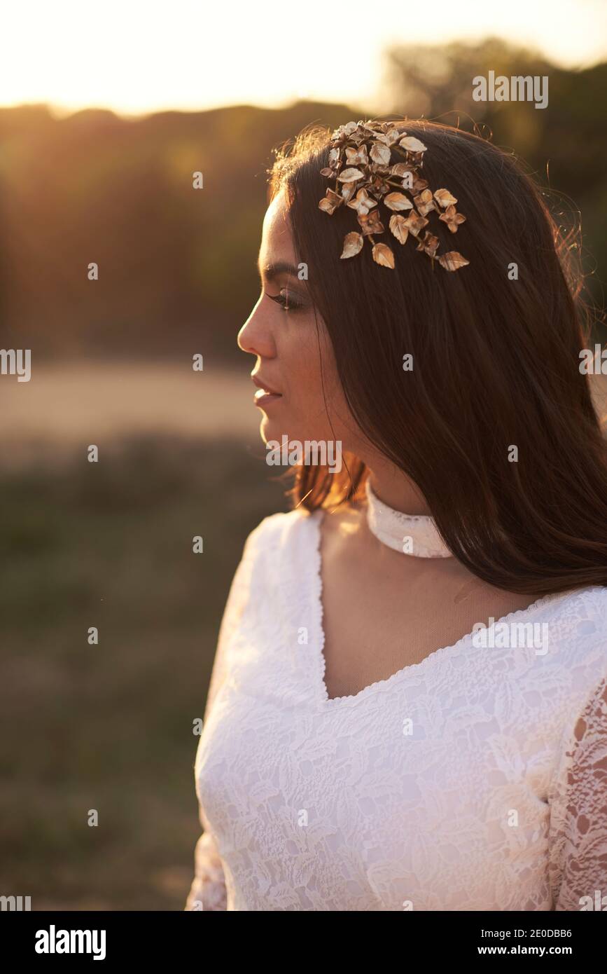 Vista laterale di elegante giovane femmina in boho bridal maxi vestitevi e cavatoie in boschi verdi e guardate via Foto Stock