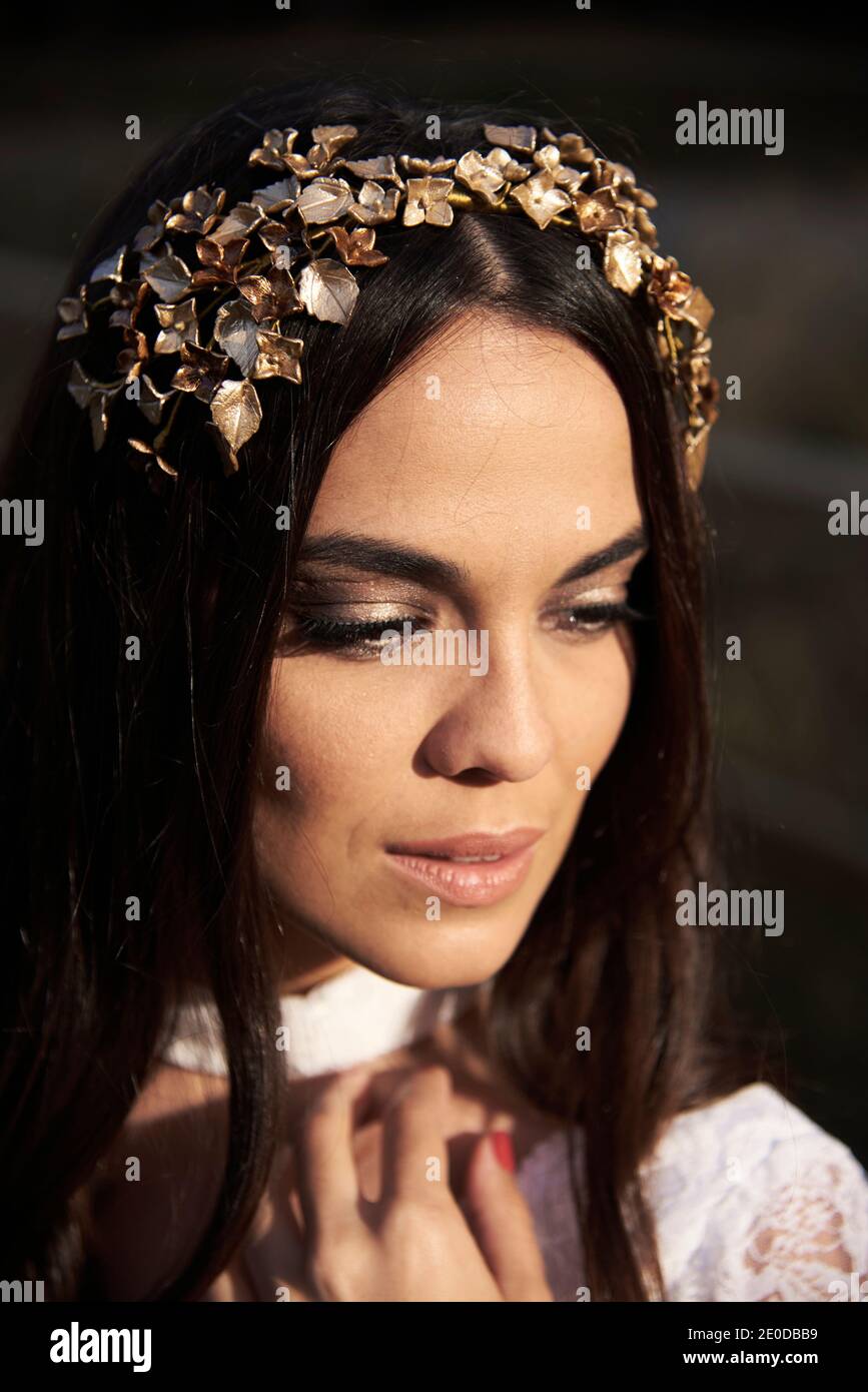Ritratto di graziosa e tenera bruna giovane in elegante pizzo bianco abito da sposa e corona da sposa che toccano la guancia Foto Stock