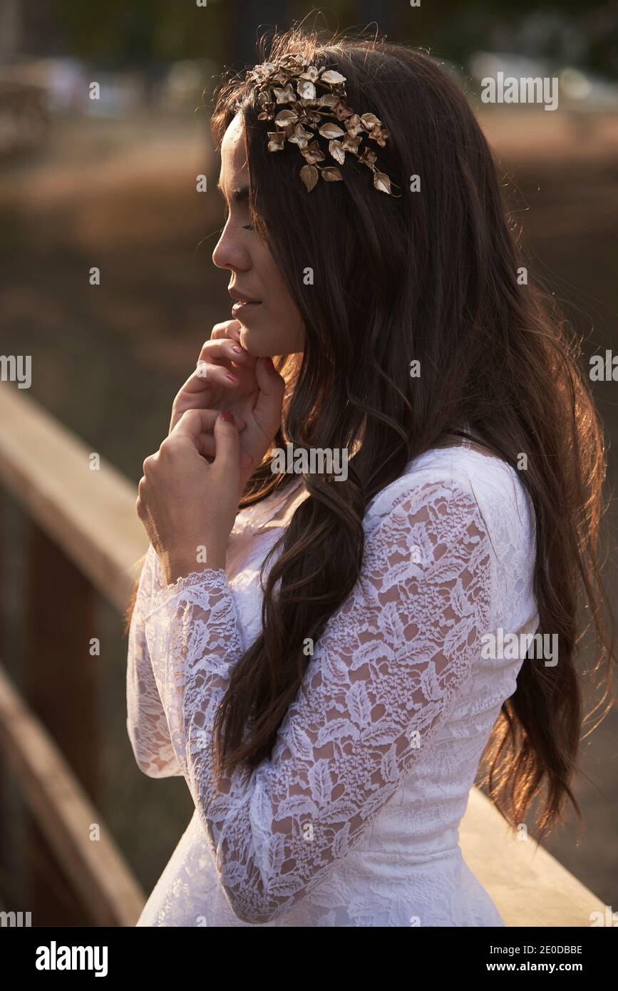 Vista laterale di elegante giovane femmina in boho bridal maxi vestitevi e cavatoie in boschi verdi e guardate via Foto Stock