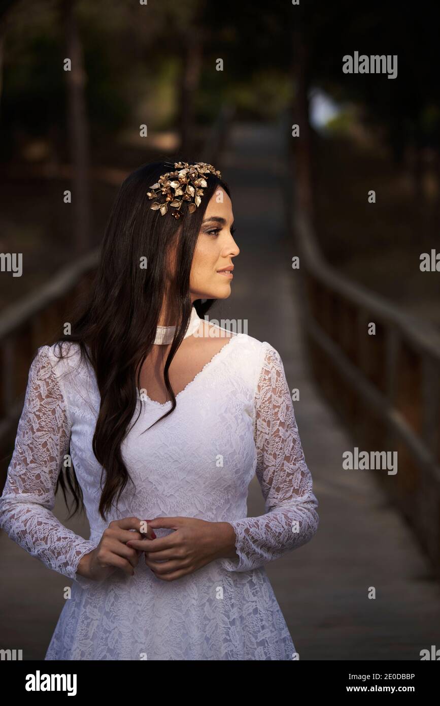Ritratto di graziosa e tenera bruna giovane in elegante pizzo bianco abito da sposa e corona da sposa che toccano la guancia Foto Stock