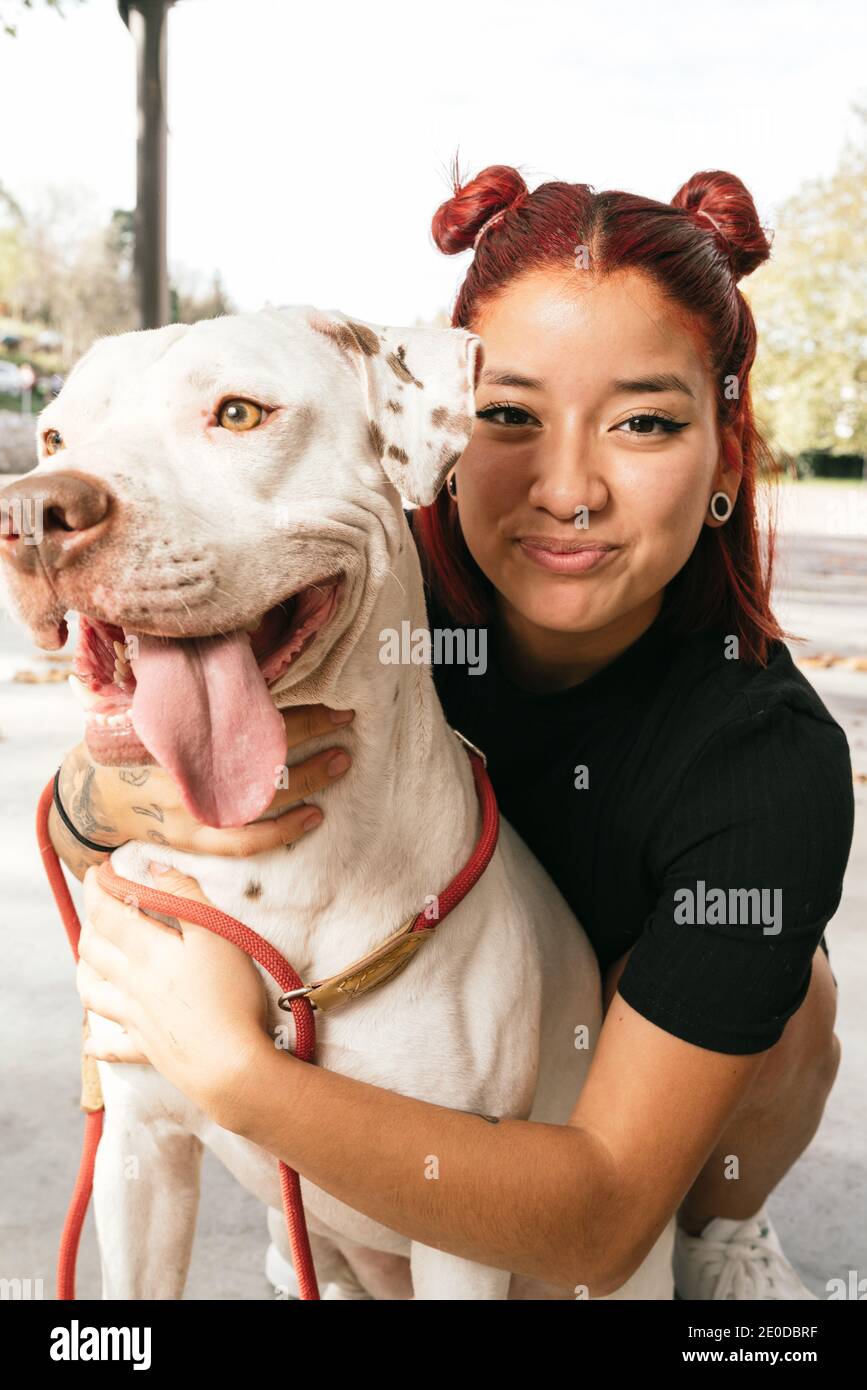 Sorridente giovane donna asiatica proprietario abbracciando obbediente purebred americano Pit Bull Terrier cane e guardando la macchina fotografica Foto Stock