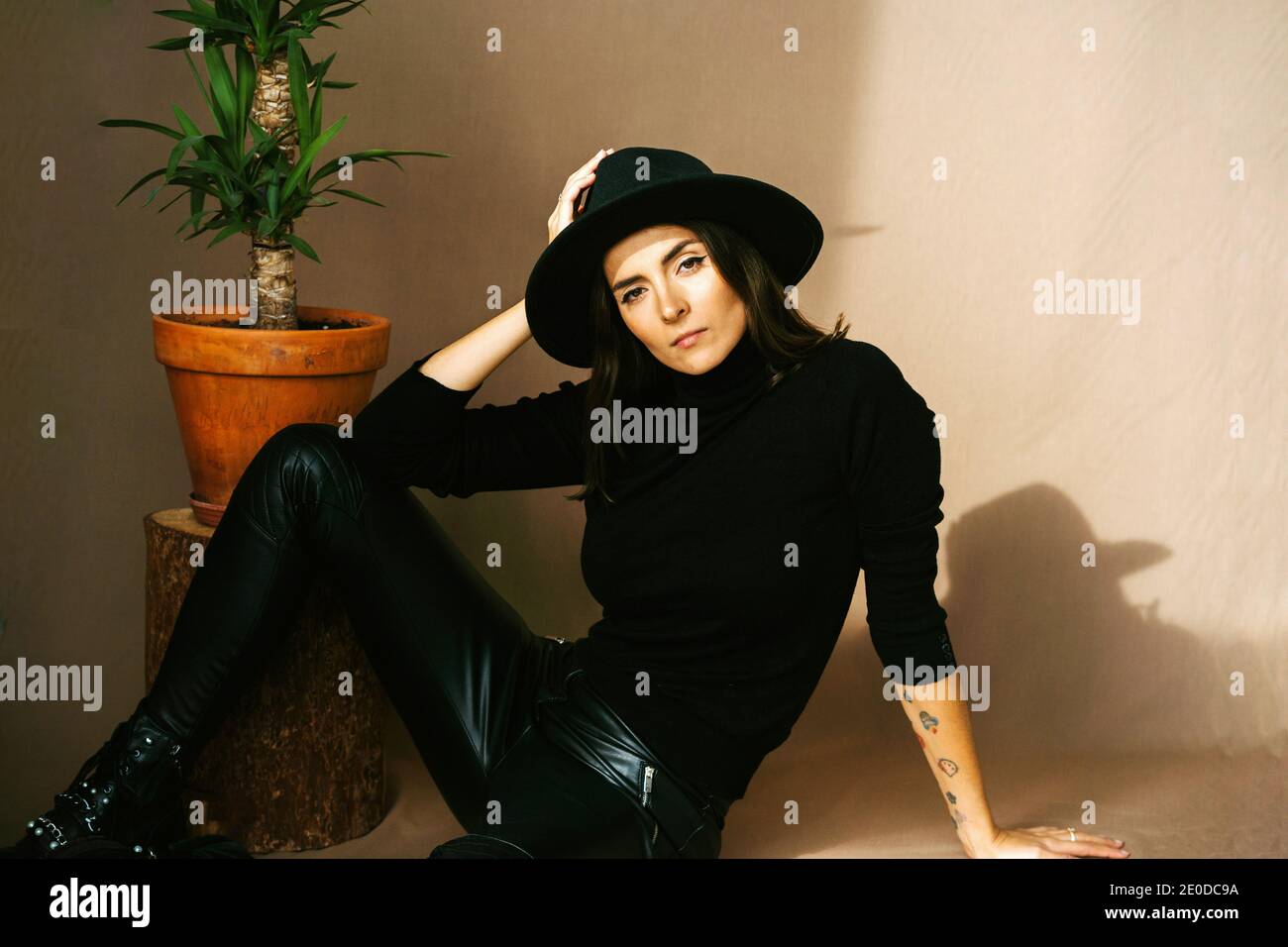 Donna giovane e sicura con tatuatura in eleganti pantaloni in pelle nera e.  dolcevita con cappello