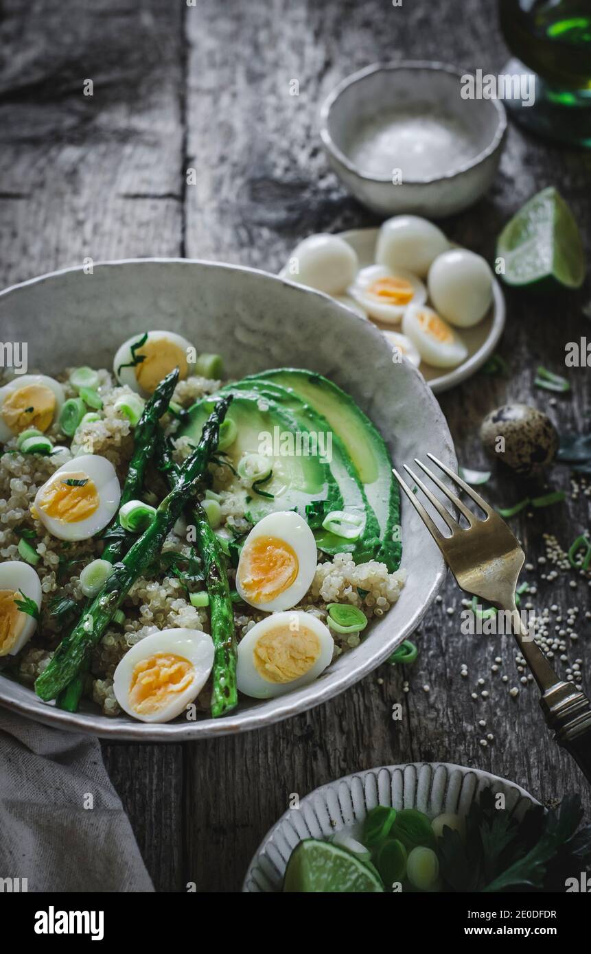 Dall'alto di deliziosa sana insalata di quinoa con uova di avocado e asparagi messi su tavola di legno con ingredienti ciotole dentro cucina Foto Stock