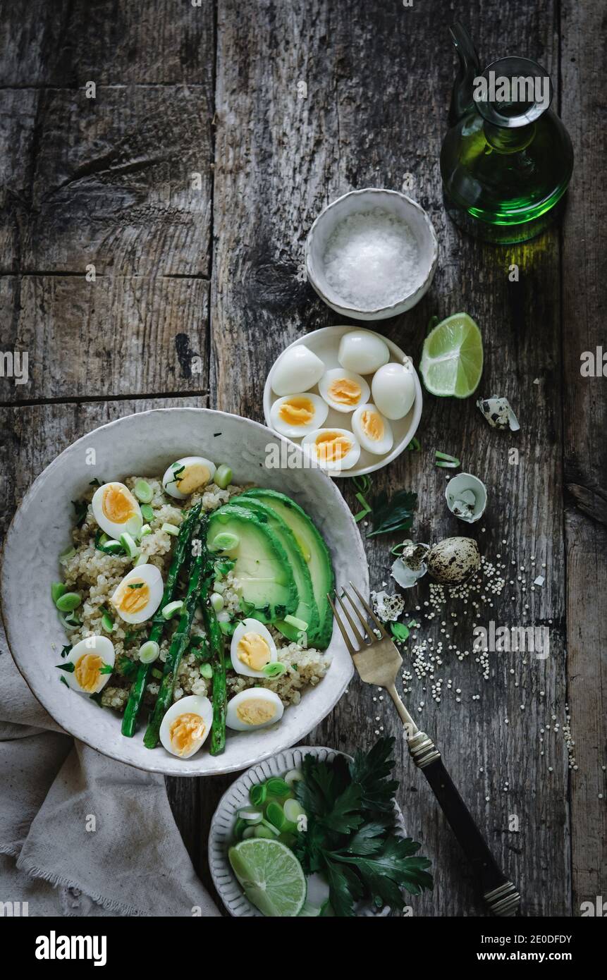 Dall'alto di deliziosa sana insalata di quinoa con uova di avocado e asparagi messi su tavola di legno con ingredienti ciotole dentro cucina Foto Stock