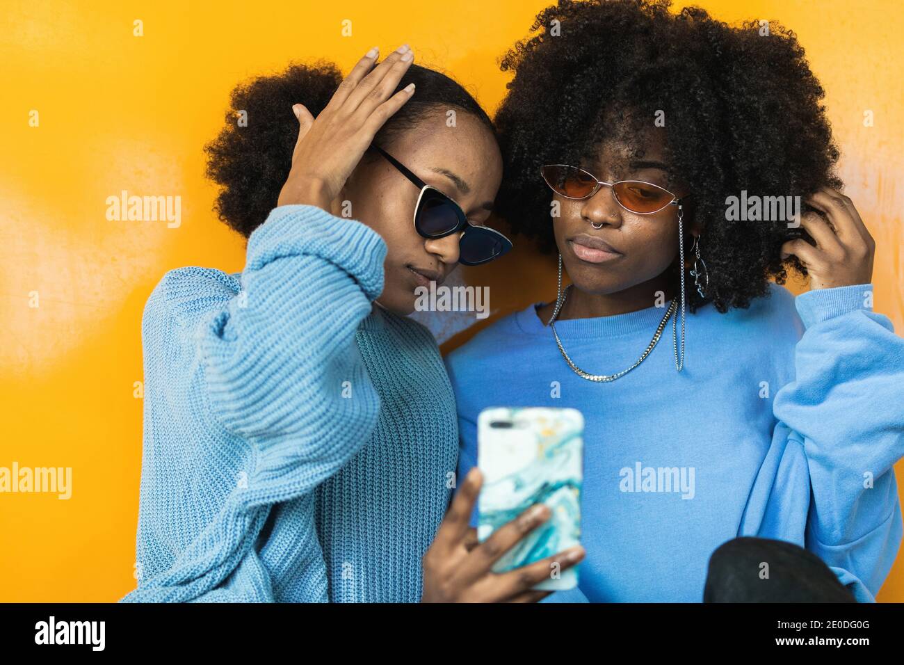 Giovani donne afroamericane in eleganti occhiali da sole e abiti lilla acquisizione di selfie sul telefono cellulare su sfondo giallo Foto Stock