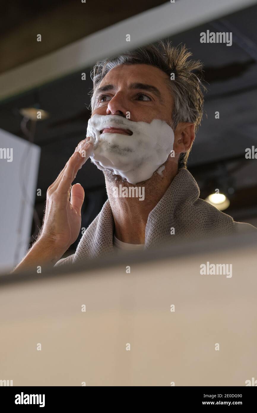 Foto di scorta di un uomo di mezza età con capelli grigi che si prepara a radersi la barba in bagno. Foto Stock