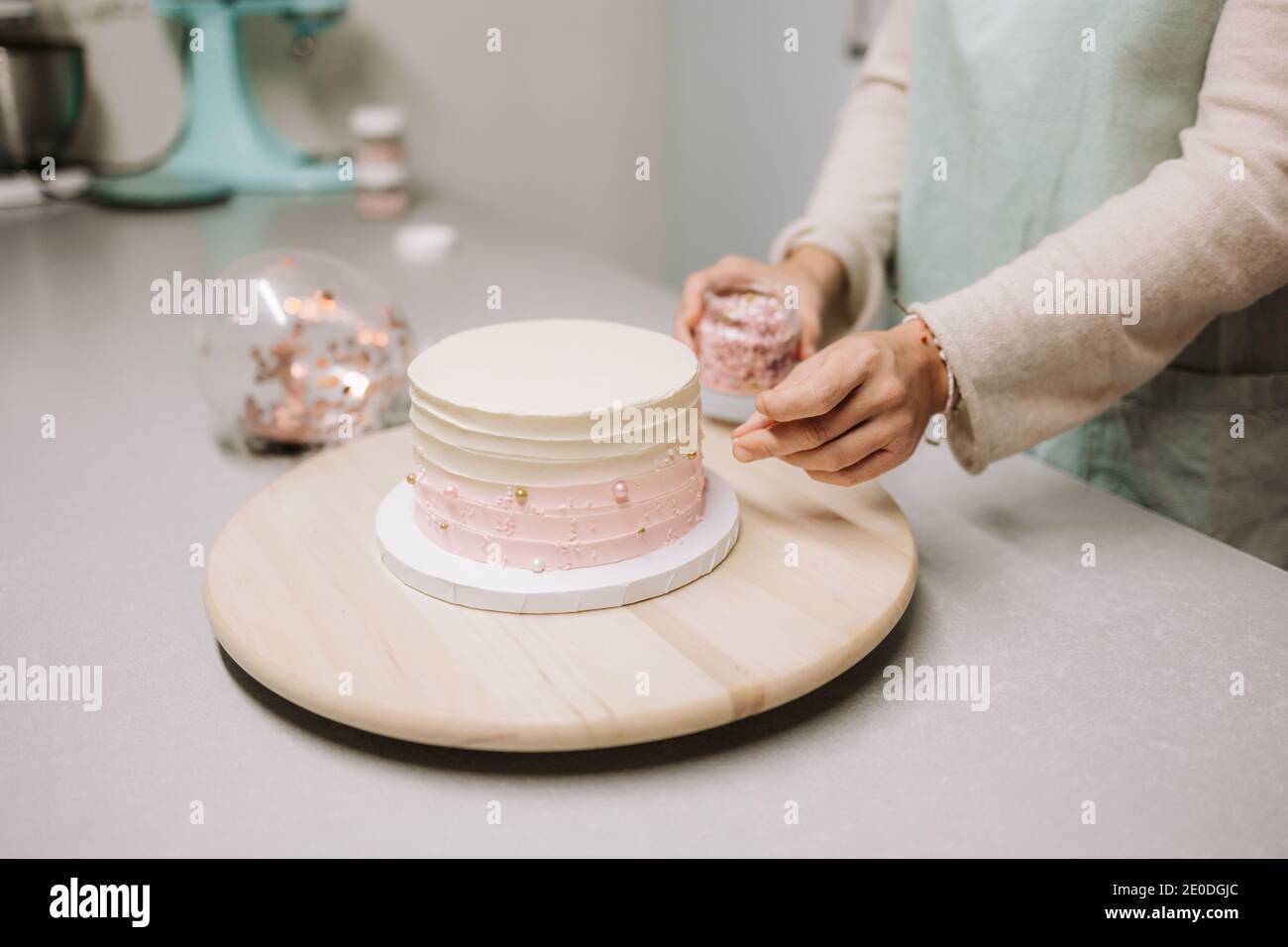 Crop anonima donna confettatrice che dispone perle commestibili su torta coperta con panna mentre si lavora al bancone in pasticceria Foto Stock