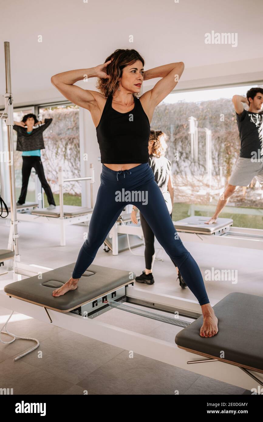 Persone in abbigliamento sportivo in piedi su pilates reformer macchine con  le mani dietro la testa e facendo esercizi durante l'allenamento Foto stock  - Alamy