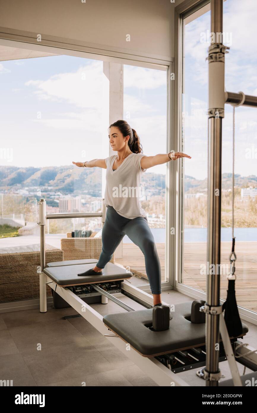 Sottile femmina in abbigliamento attivo facendo yoga in Warrior posa su  pilates riformatore in palestra e guardando via Foto stock - Alamy