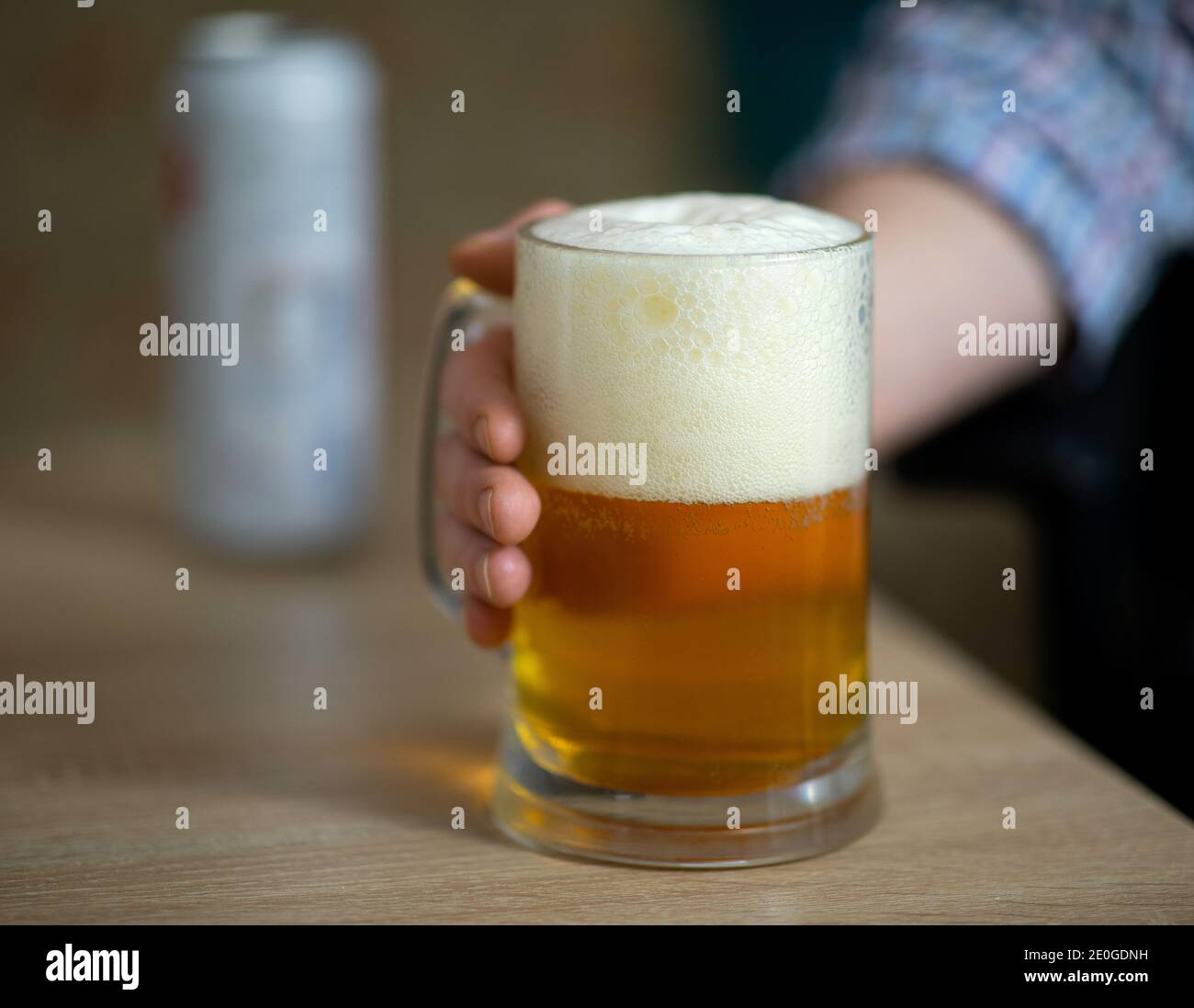 Mano maschile che tiene grande tazza piena di birra fresca alcolica su sfondo di legno, uomo a casa, fuoco selettivo Foto Stock
