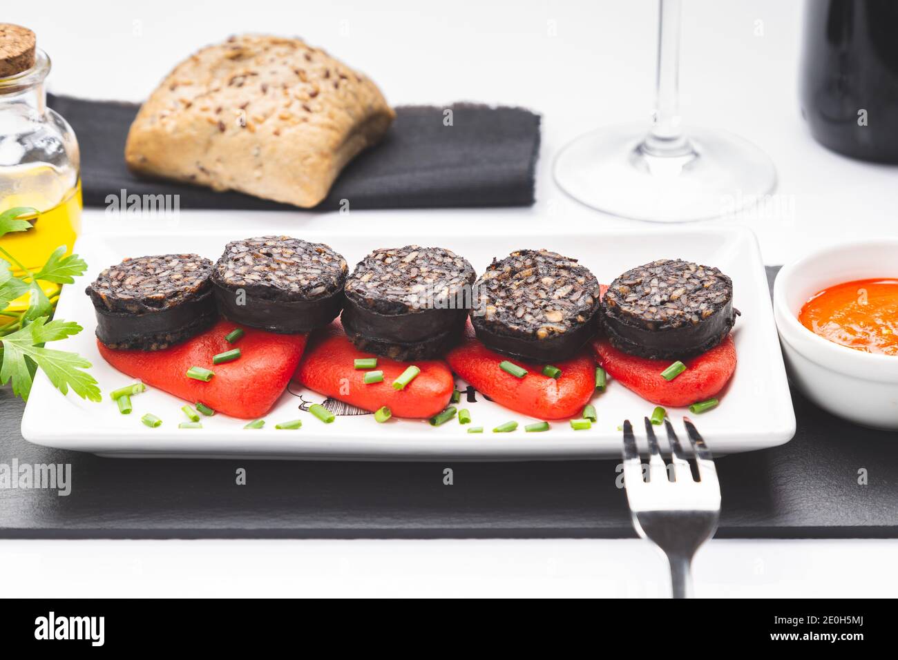 Fette di budino nero spagnolo su peperoni piquillo in piatto bianco su sfondo bianco. Tapas spagnole. Foto Stock