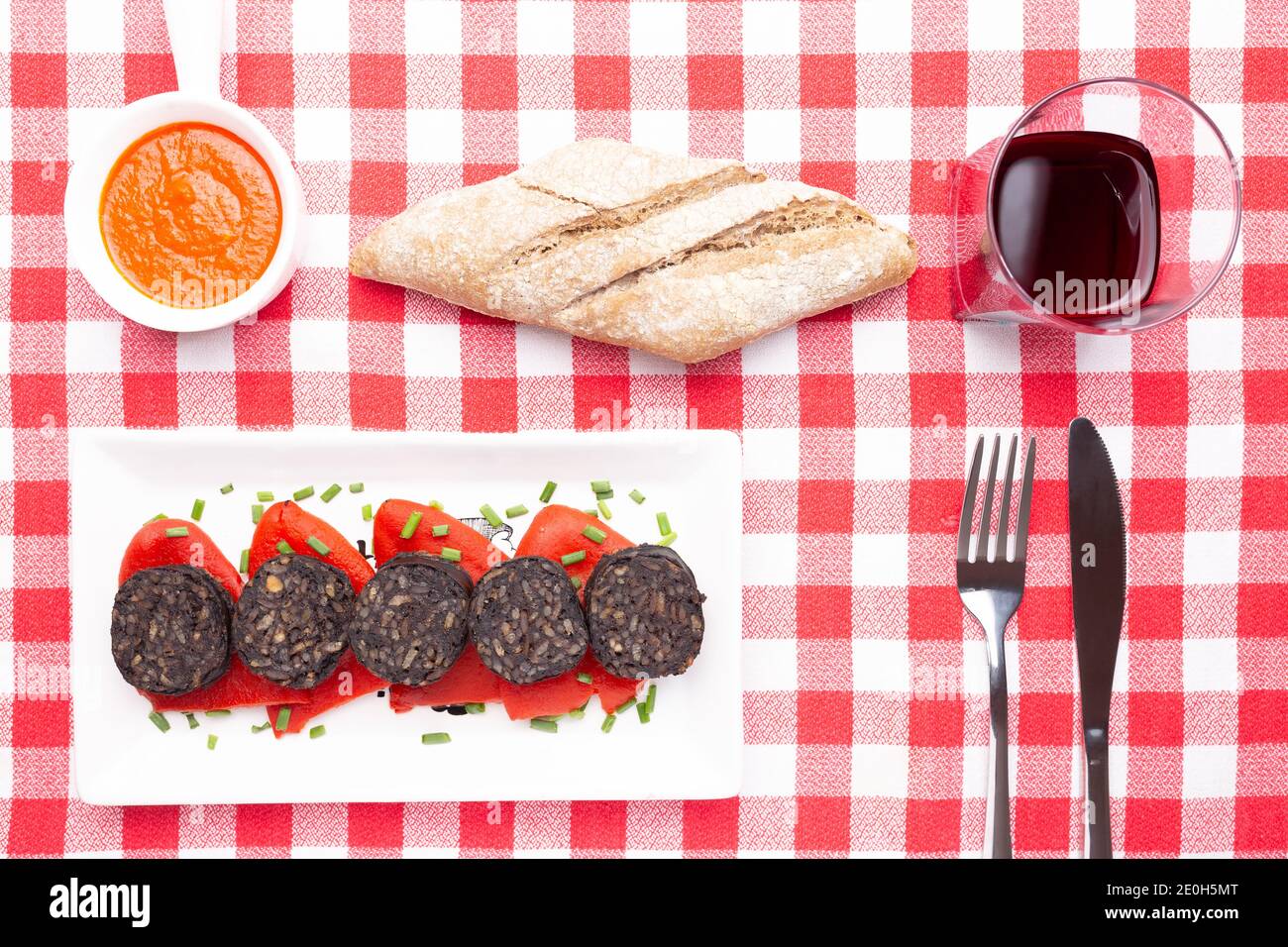 Fette di pudding nero spagnolo su peperoni piquillo in piatto bianco su una tovaglia a scacchi rossi . Tapas spagnole. Foto Stock