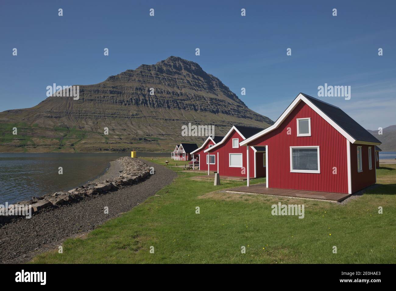 Casa tradizionale con pannelli in legno dipinto di rosso con la possente montagna di Holmatindur sullo sfondo a Eskifjordur, Islanda orientale. Foto Stock