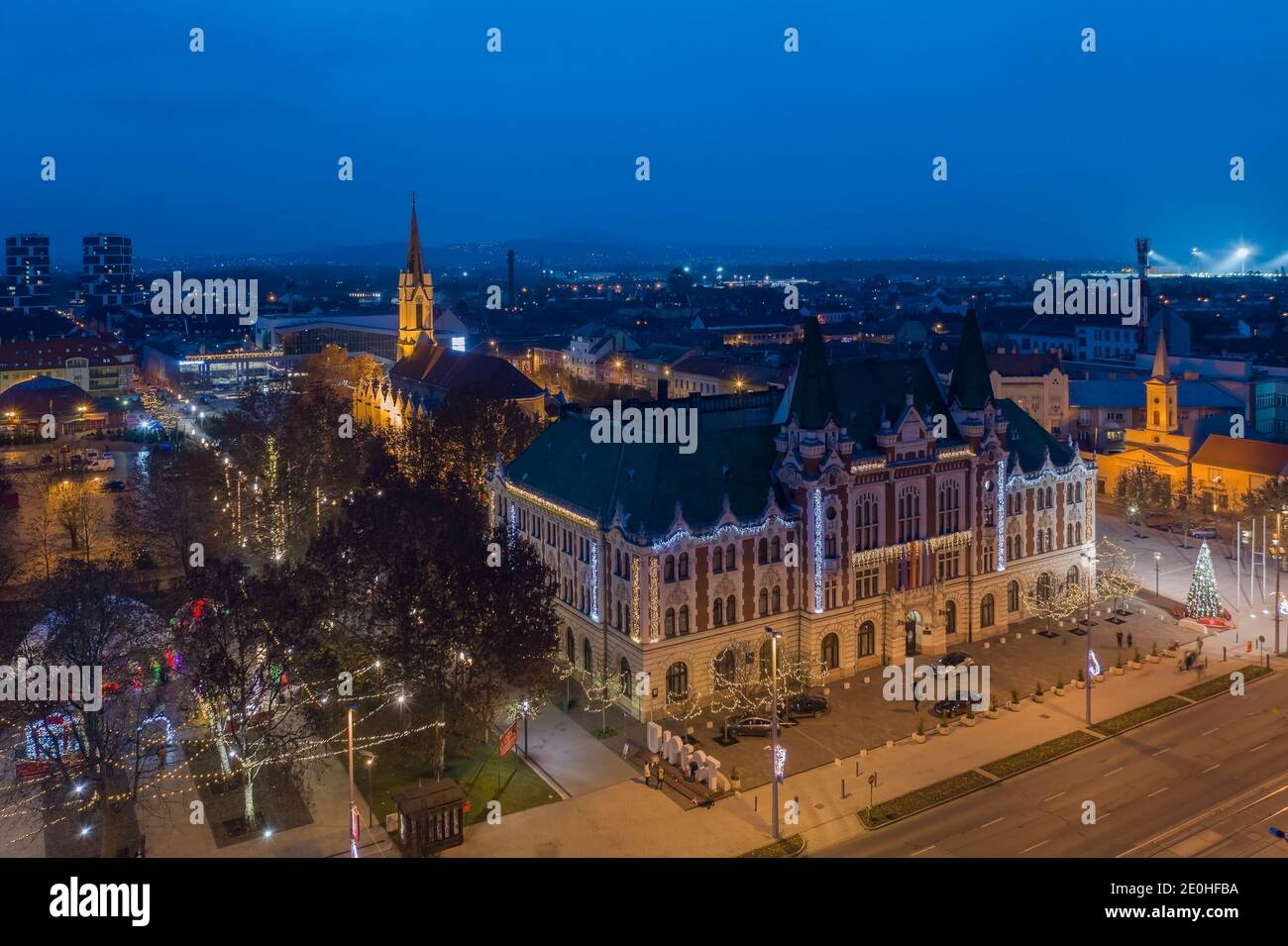 Újpest, Budapest, Ungheria - veduta aerea del municipio di Ujpest con la chiesa della Regina del Cielo e le luci di Natale. Paesaggio urbano dell'ora blu. Újpest Városháza Foto Stock