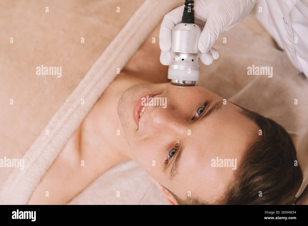 Vista dall'alto da vicino di un bell'uomo allegro che ha trattamento viso rassodante per la pelle presso il salone di cosmetologia Foto Stock