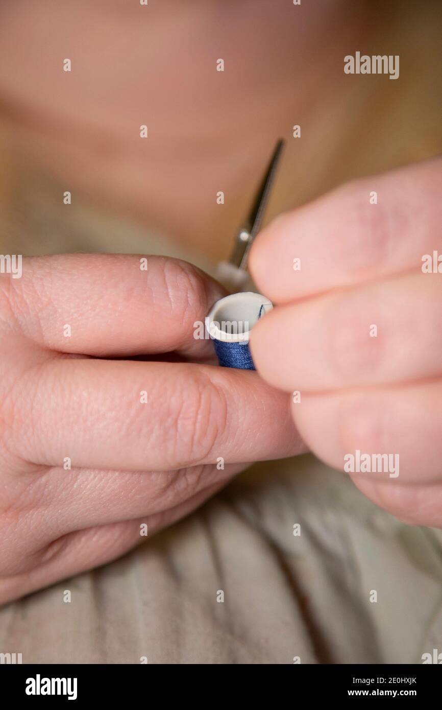 Donna che tira filo blu, preparandosi a tagliarlo Foto Stock