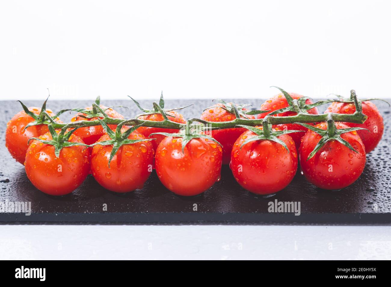 Pomodori ciliegini freschi sul ramo, su lavagna isolata su sfondo bianco. Foto Stock