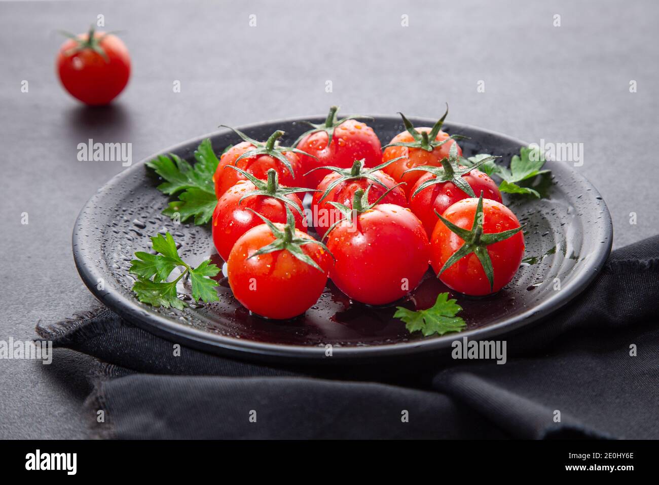 Pomodori ciliegini freschi su piatto nero rotondo, su fondo scuro. Foto Stock