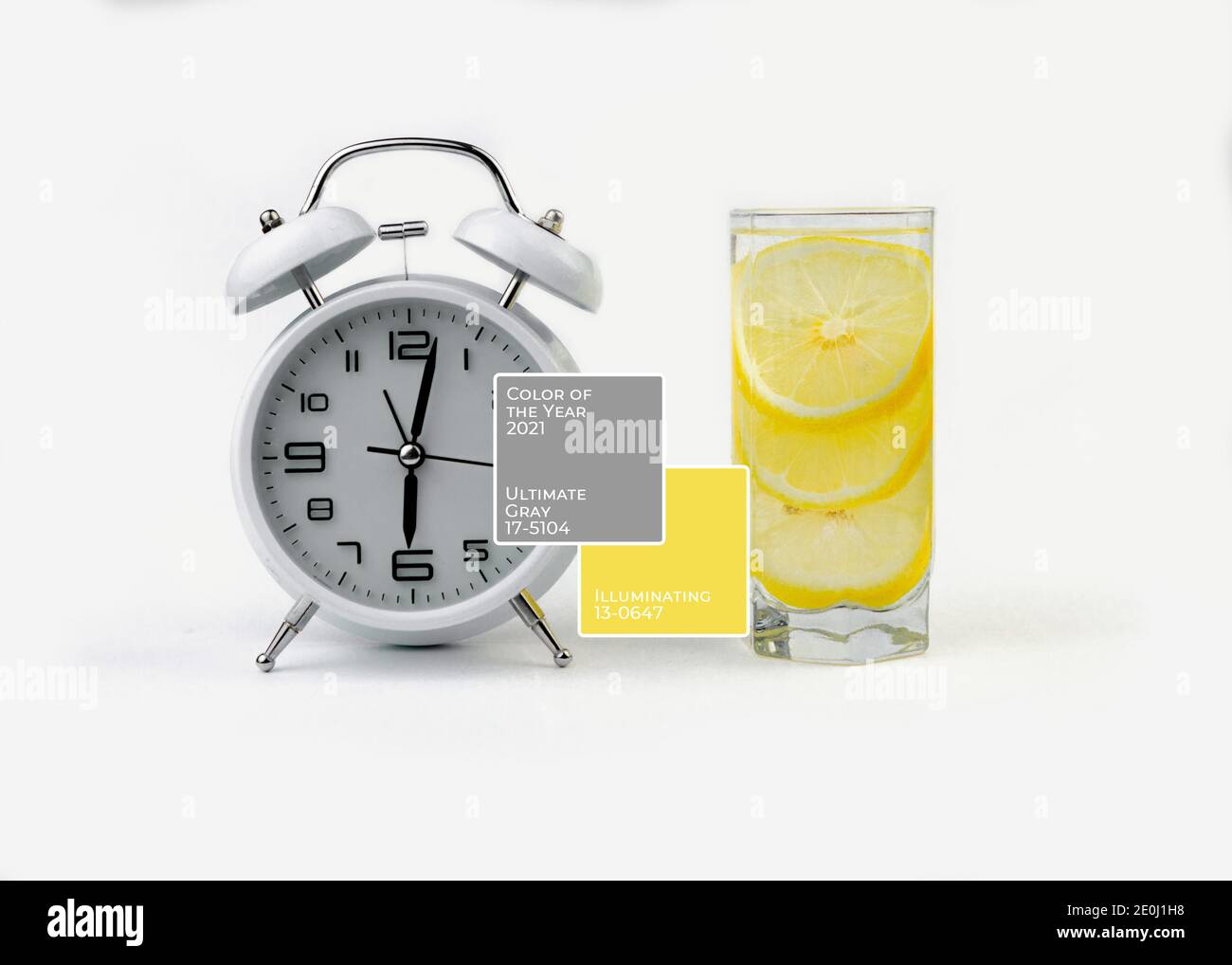 Bicchiere d'acqua con limone e sveglia. Colore dell'anno 2021. Illuminazione e Ultimate Grey. Sfondo giallo e grigio, Foto Stock