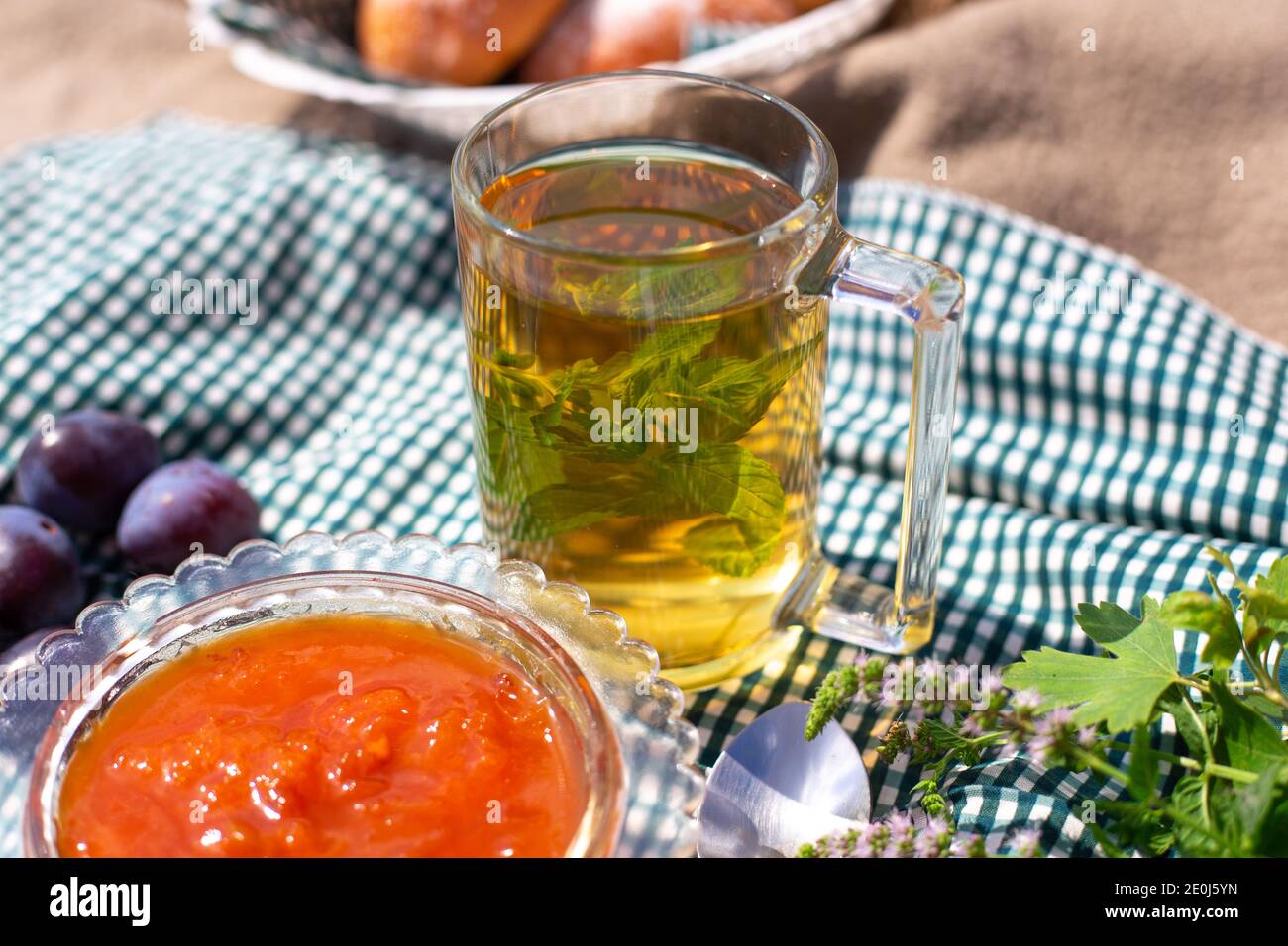 Una tazza di tè caldo con menta in un bicchiere trasparente, accanto ad un vaso con marmellata di frutti di bosco all'aria aperta. La vita still stagionale, il tè del mattino, il riposo domenicale. Foto Stock