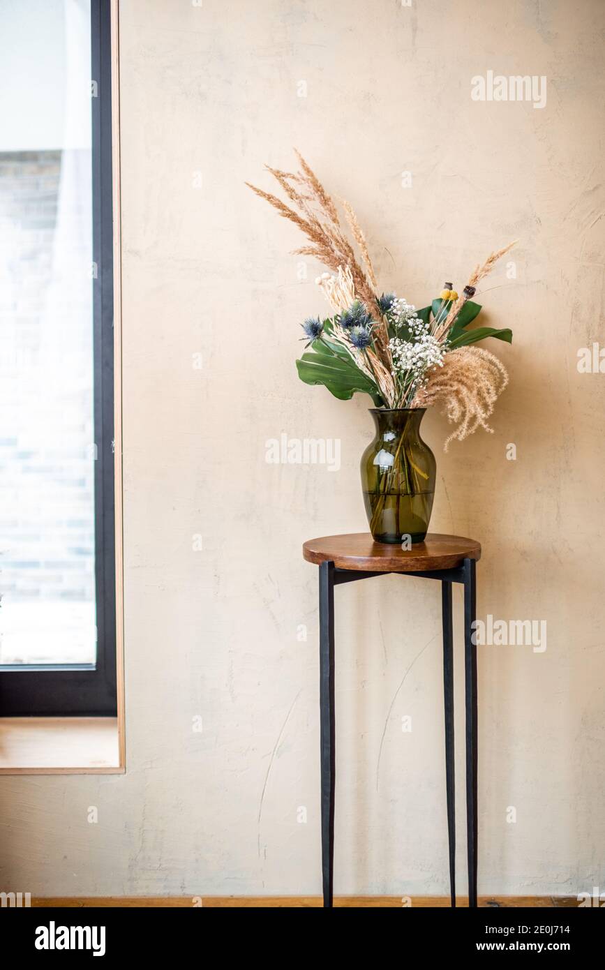 Composizione di fiori ed erbe in vaso di vetro su fondo beige. Bouquet di piante di monstera, Craspedia, Miscanto, Erngium, Brunia, Gypsophila Foto Stock