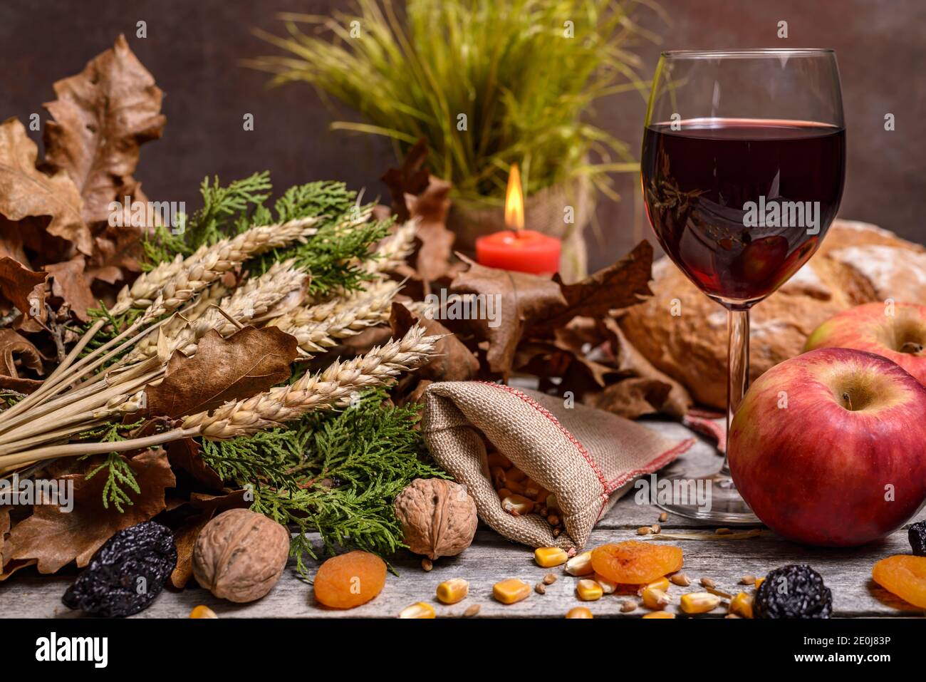 Cibo tradizionale per la vigilia di Natale ortodossa. Tronchi di Yule o badnjak, vino, pane, mele, cereali, frutta secca e candela in fiamme su tavola rustica. Conce Foto Stock