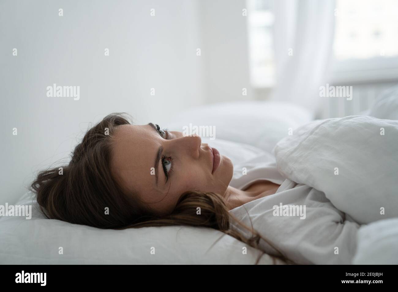 Donna arrabbiata seccata da vicini rumorosi, guardando in su, sofferente da insonnia o dallo sforzo. Donna stanca che cerca di addormentarsi a letto a casa in anticipo Foto Stock