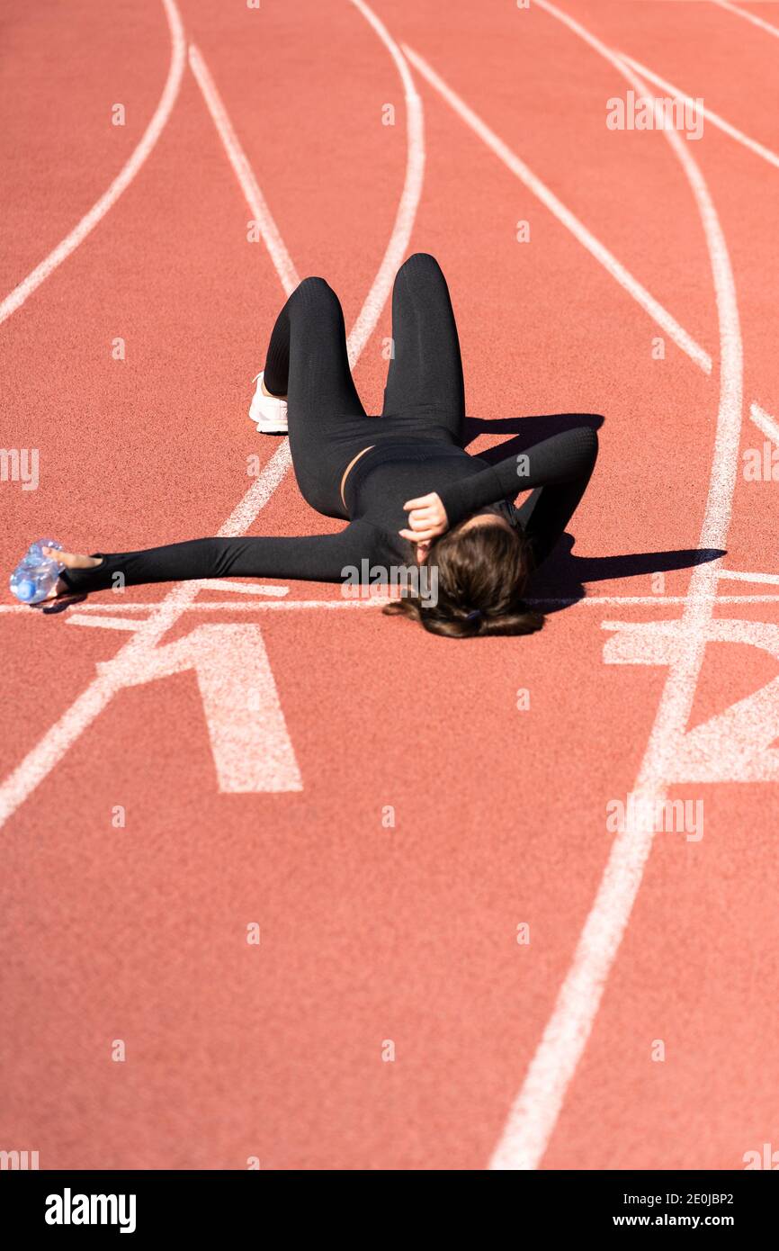 Vista dall'alto di una donna stanca in forma sportiva che riposa dopo l'allenamento o che corre su uno stadio di gomma tapis roulant, tenendo una bottiglia d'acqua, facendo una pausa du Foto Stock