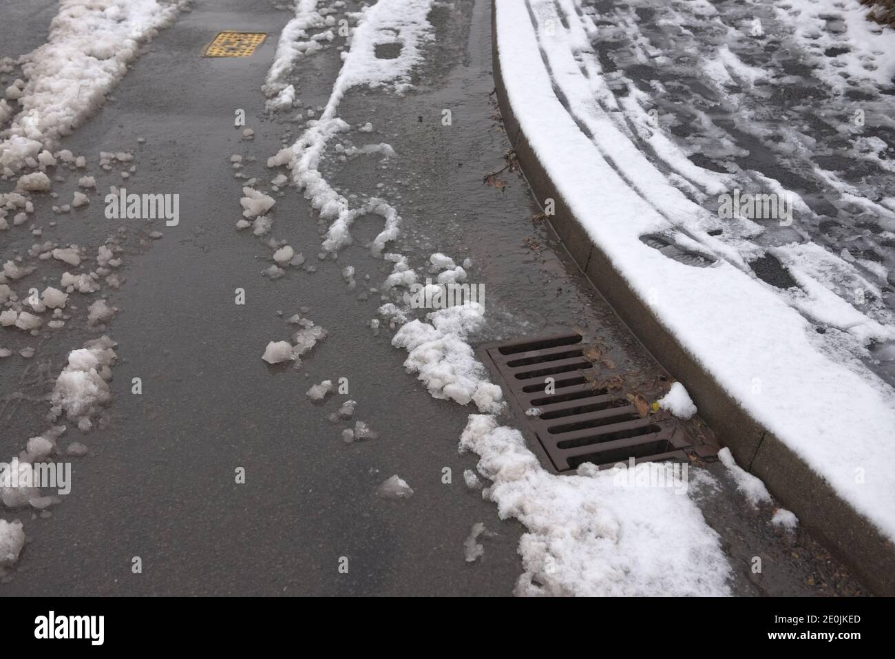 8 - scarico di superficie all'angolo di una strada asfaltata, circondata da nevicate che si fondono. Ambiente invernale nel Regno Unito e infrastrutture di gestione delle acque. Foto Stock