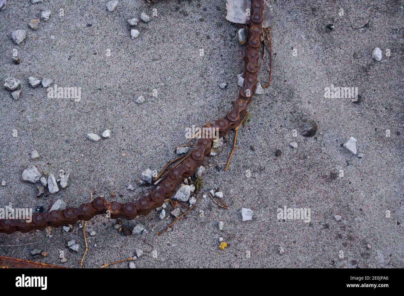 Primo piano foto di una lunghezza di catena arrugginita e ghiaia su cemento. Foto Stock