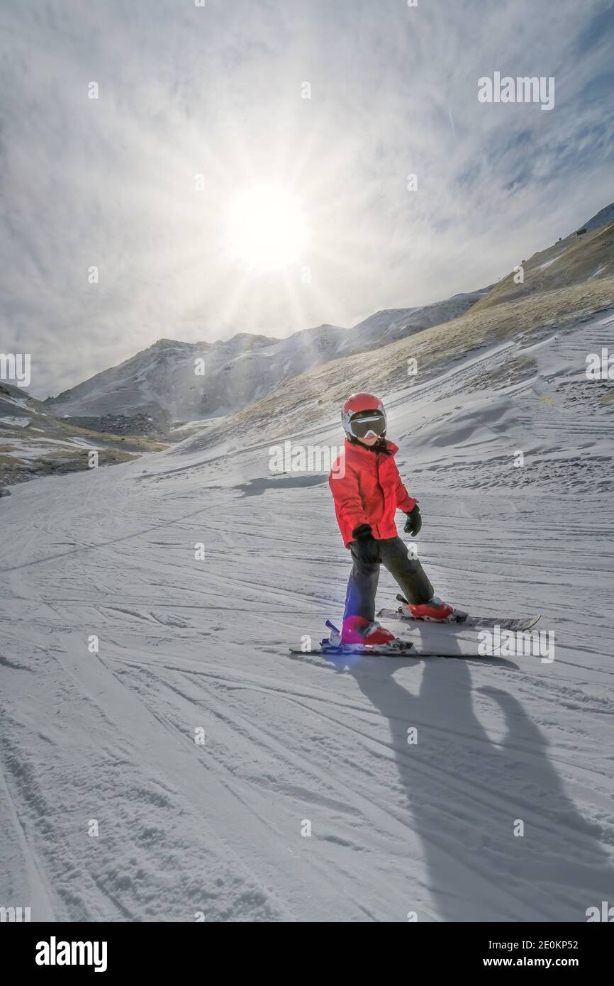 Bambino con casco e giacca rossa impara a sciare con il sole sullo sfondo, nella stazione sciistica di Boi Taull, Pirenei Lleida, Spagna, verticale Foto Stock