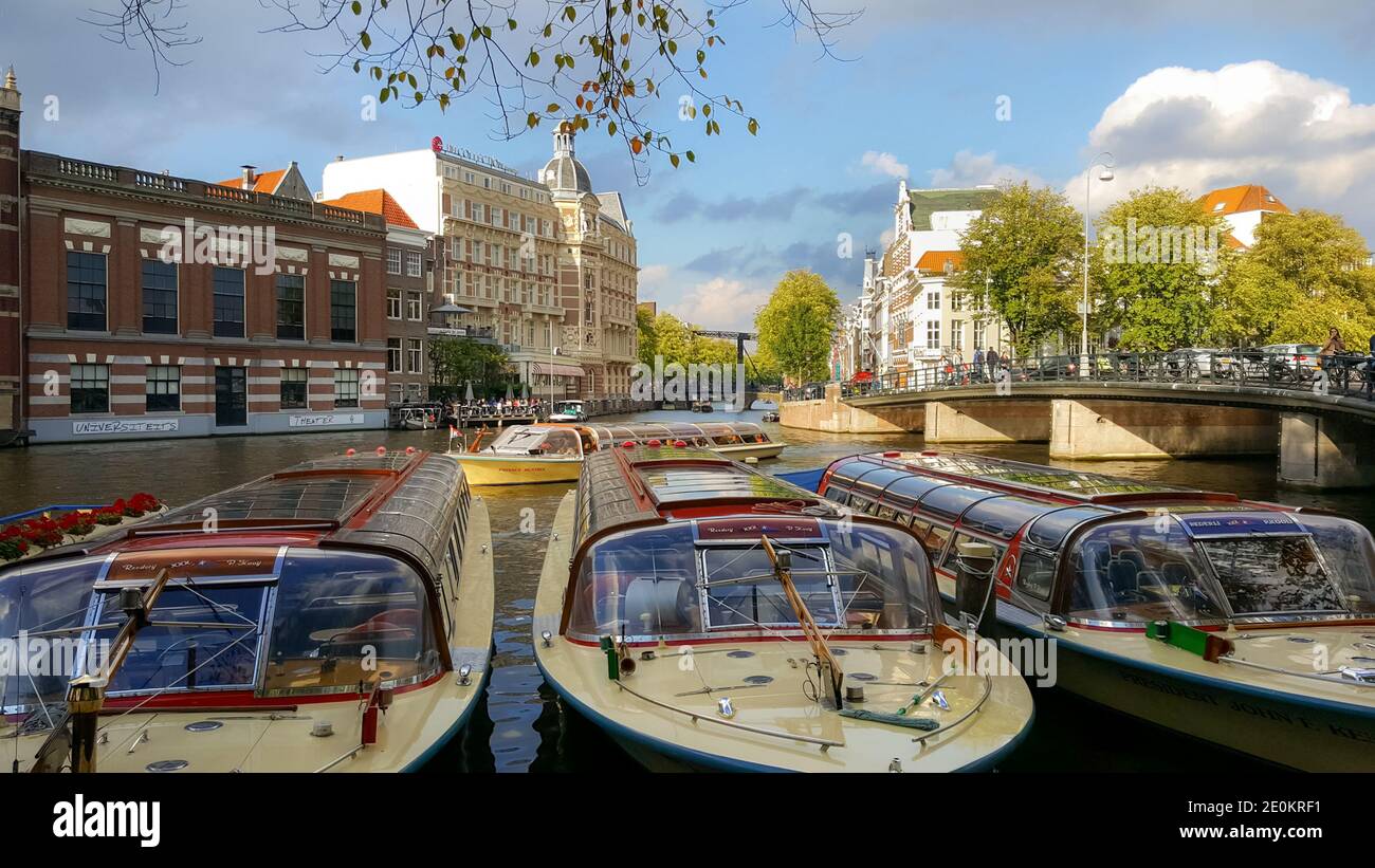Le colorate barche gialle e rosse aspettano i passeggeri di turisti su un canale principale di Amsterdam, Paesi Bassi Foto Stock
